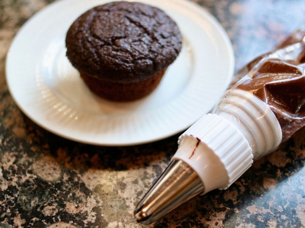 Gluten-free vegan chocolate cupcake on a plate with a piping bag full of chocolate frosting.