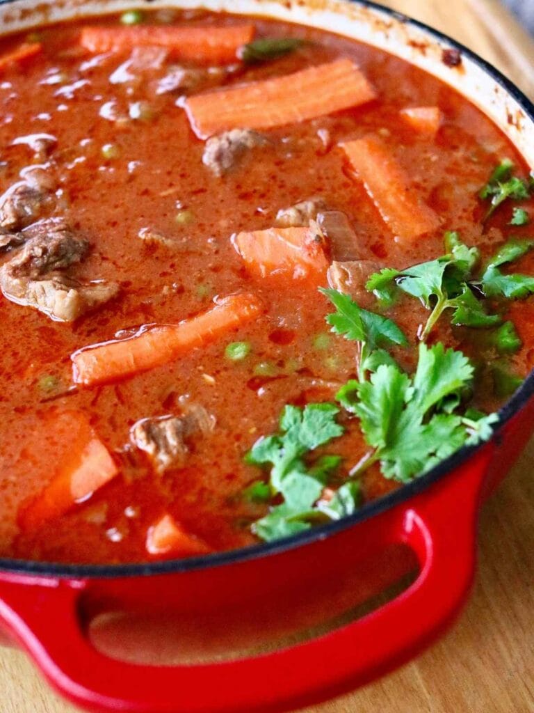 Indian beef curry in a ceramic dutch oven with cilantro on top.