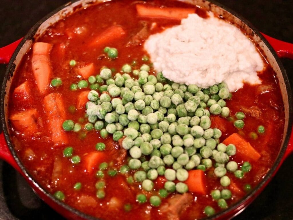 Adding peas and coconut cream to curry in a Dutch oven.