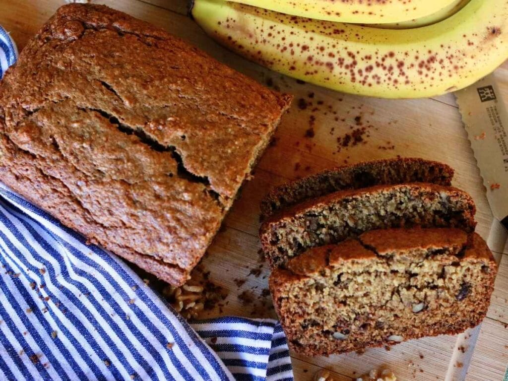 Two slices of oat flour banana bread cut from loaf with bananas in the background.