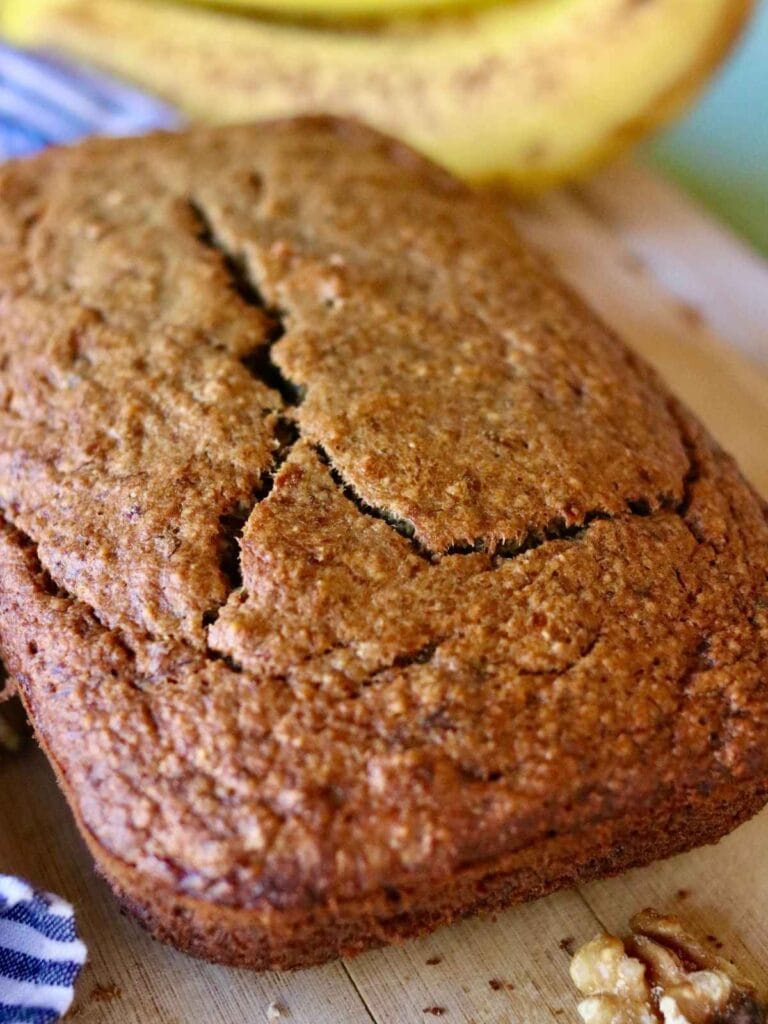 Loaf of oat flour banana bread on a cutting board with bananas in the background.