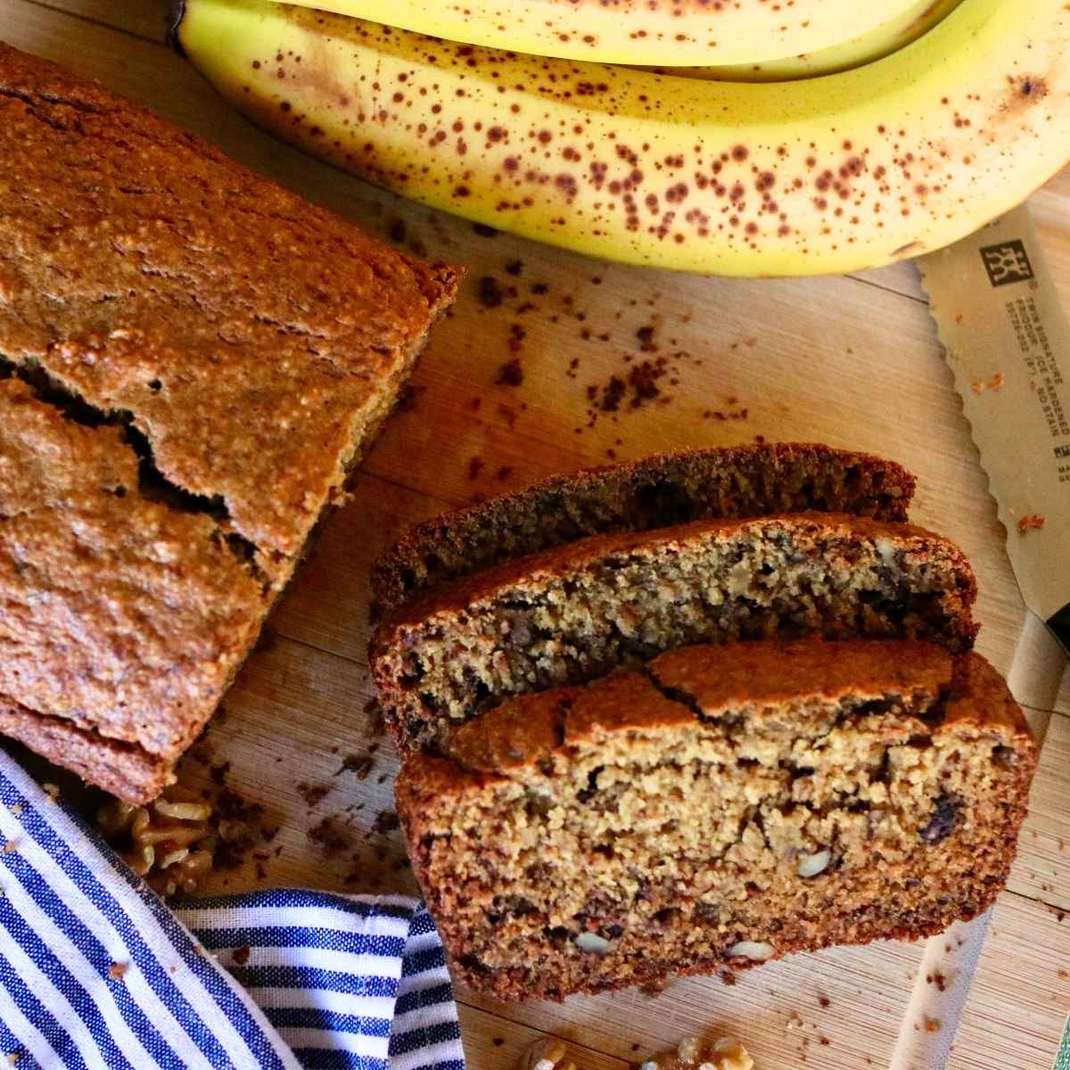 Two slices of oat flour banana bread cut from loaf with a knife and bananas.