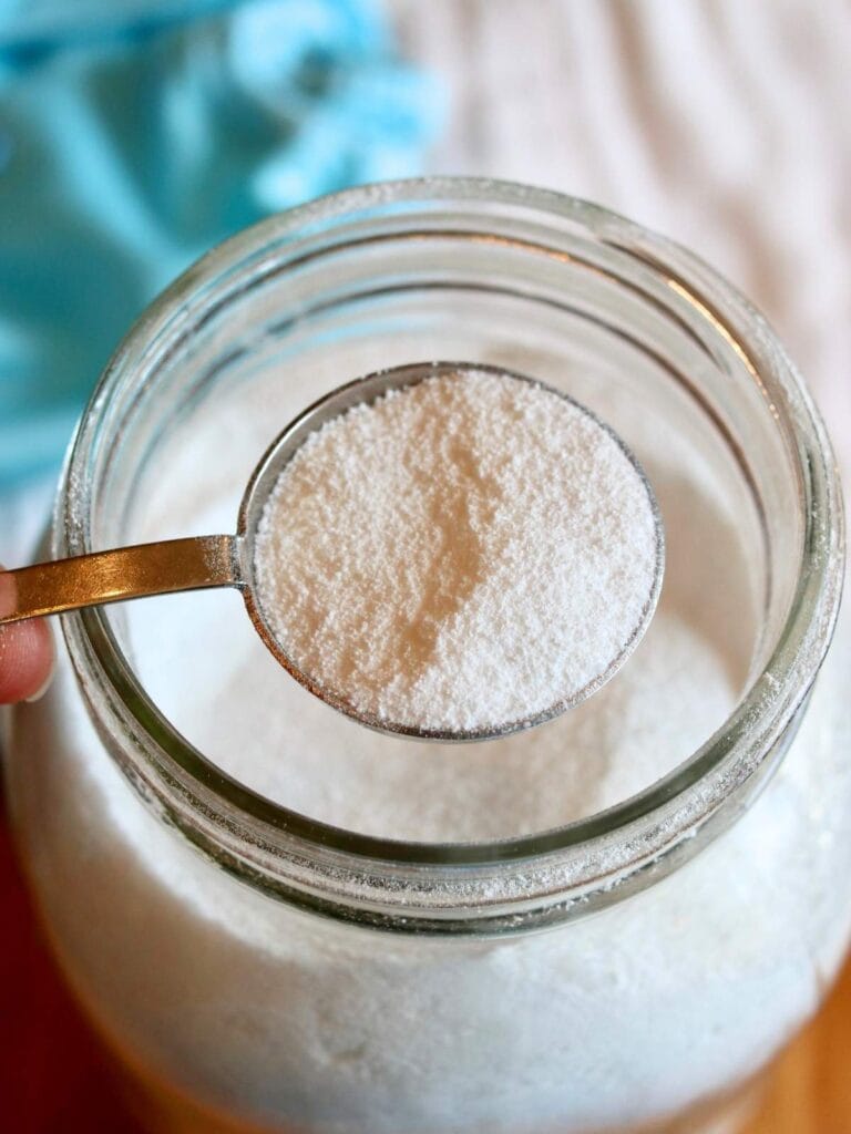 Scooping a tablespoon of cloth diaper detergent out of a glass jar.
