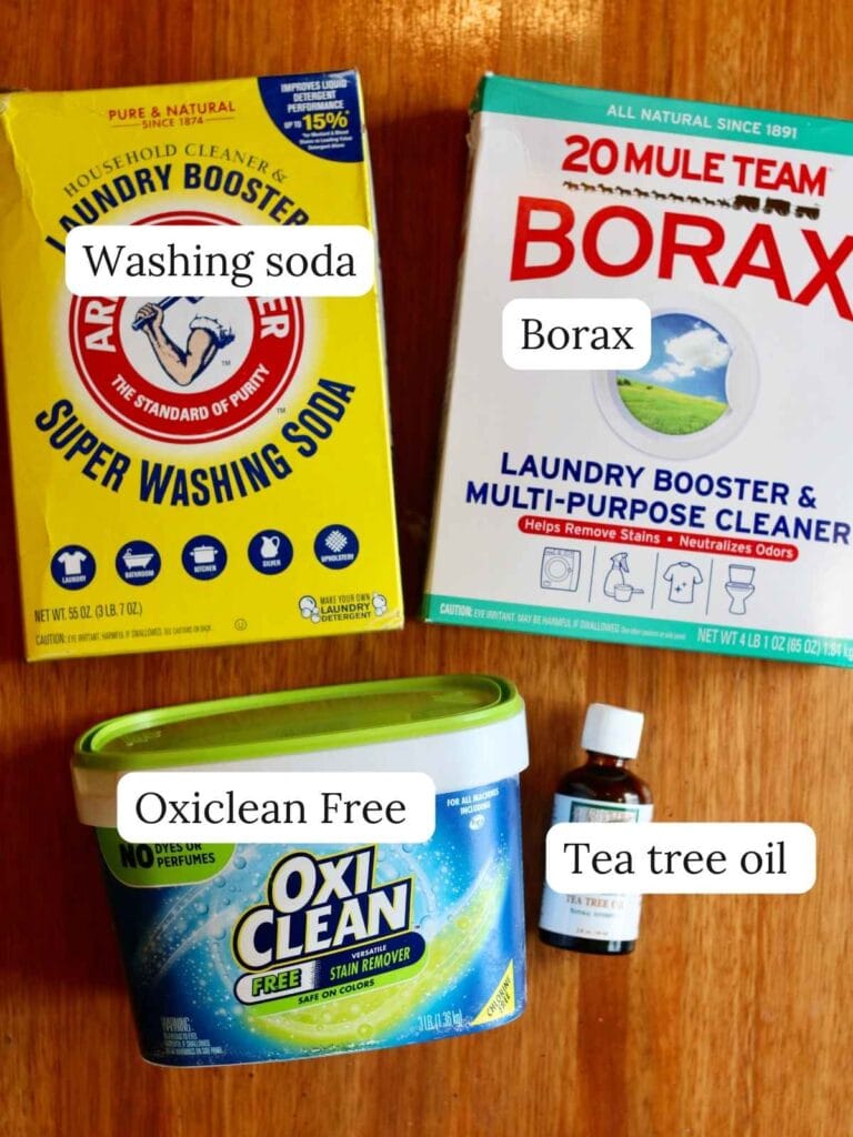 Ingredients for cloth diaper detergent including oxiclean free, tea tree oil, borax, and washing soda on a wood background.