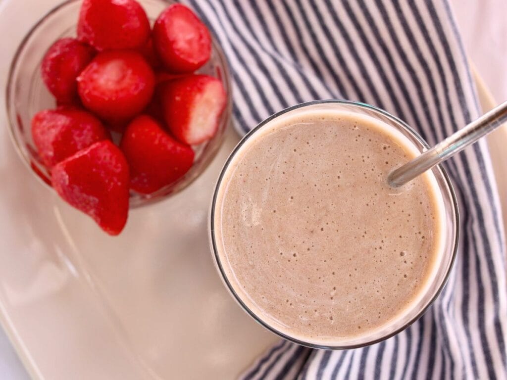 Ginger smoothie in a glass with a bowl of strawberries and a cloth napkin.