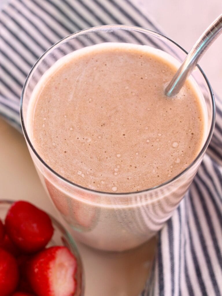 Ginger smoothie in a glass with a straw with a bowl of strawberries.