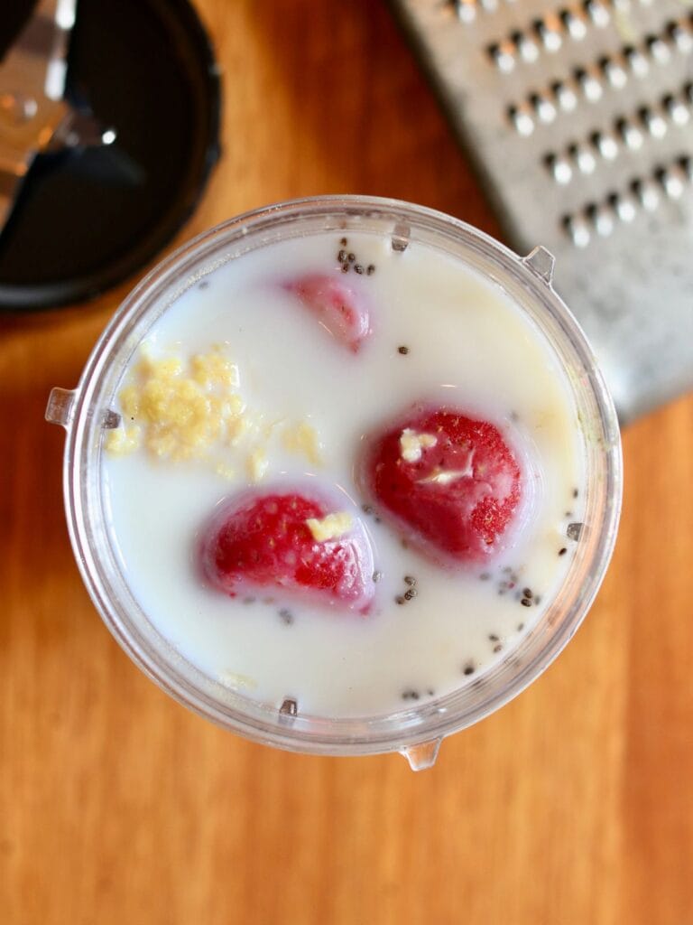 Milk, strawberries, ginger, and other ingredients in a blender cup.