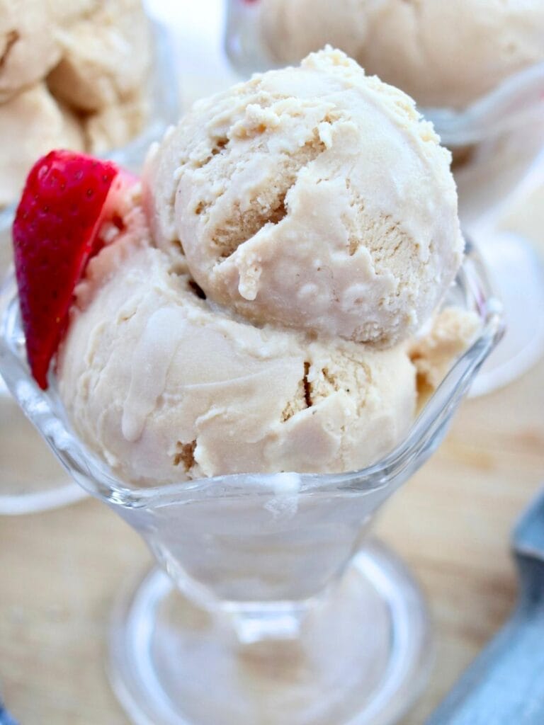 Closeup of bowl with two scoops of ice cream and half of a strawberry.