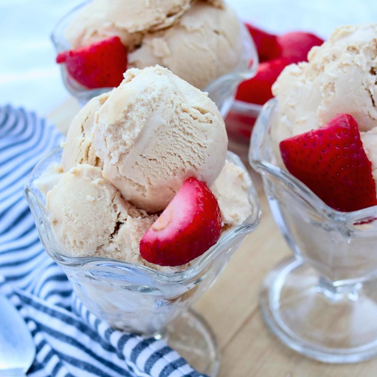 Three glass ice cream bowls filled with ice cream and garnished with strawberries.