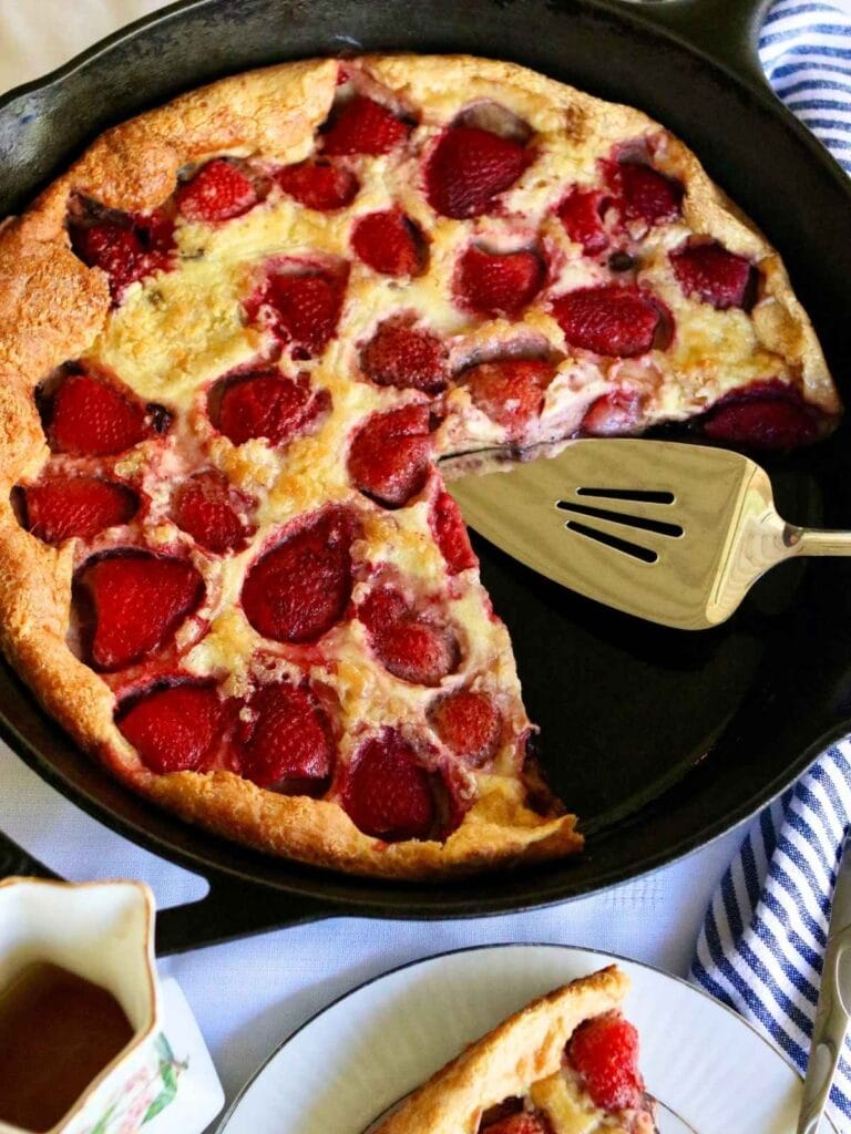 Skillet with strawberry Dutch baby with a few slices taken out.