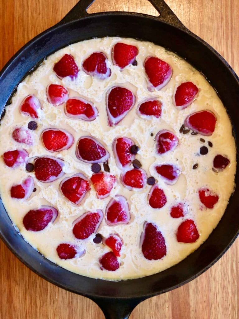 Batter with strawberries and chocolate chips in a cast iron skillet.