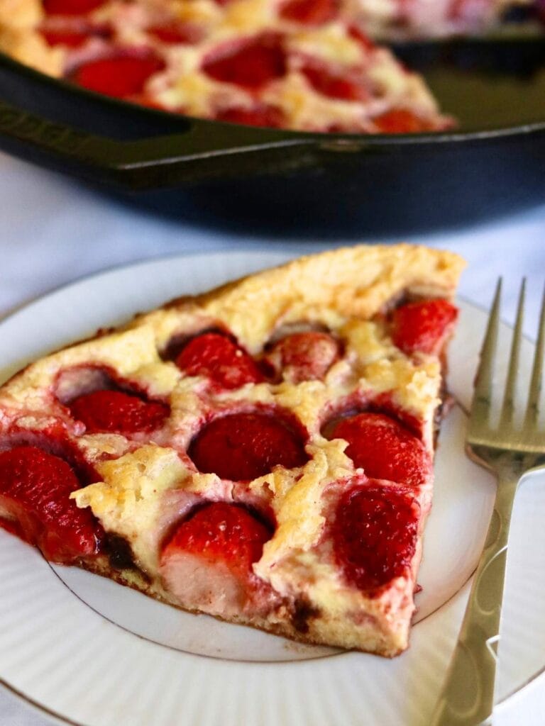 Slice of strawberry Dutch baby on a plate with a fork.