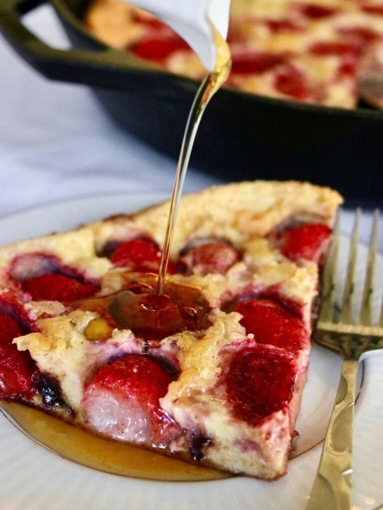 Syrup pouring on a slice of strawberry Dutch baby.