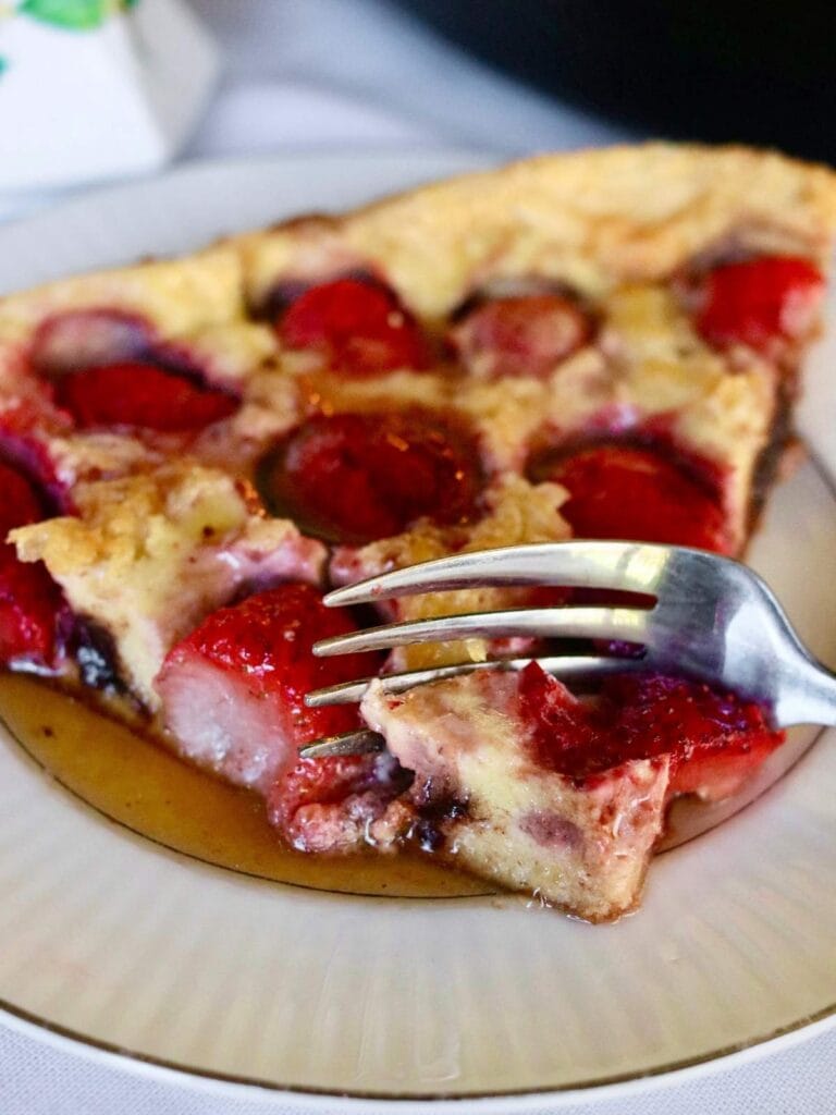 Fork taking a bite out of a slice of strawberry Dutch baby.