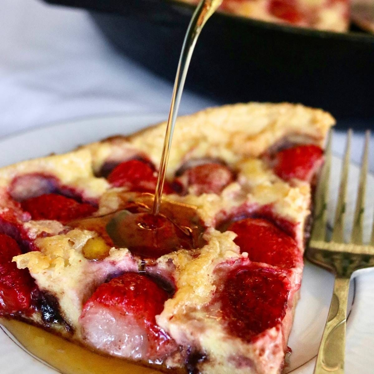 Closeup of syrup pouring on a slice of strawberry Dutch baby.