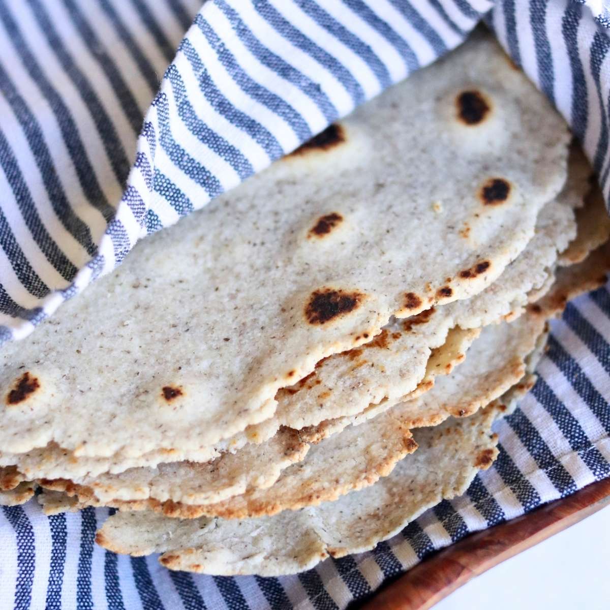 Almond flour tortillas wrapped in cloth in a wooden bowl.