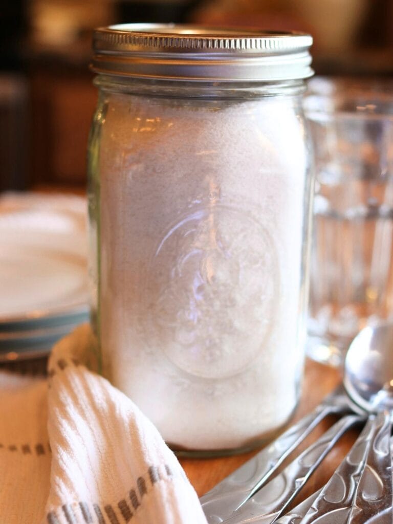 Mason jar with homemade dishwasher detergent with variety of clean dishes.