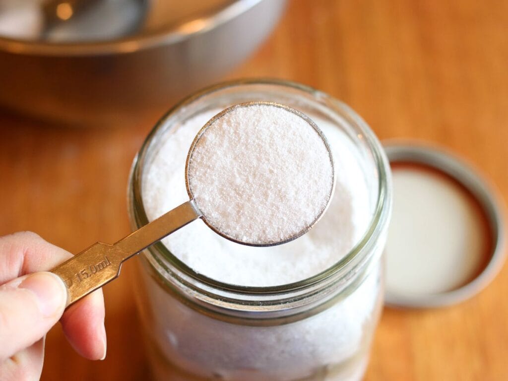 Tablespoon of homemade dishwasher detergent scooped out of Mason jar.