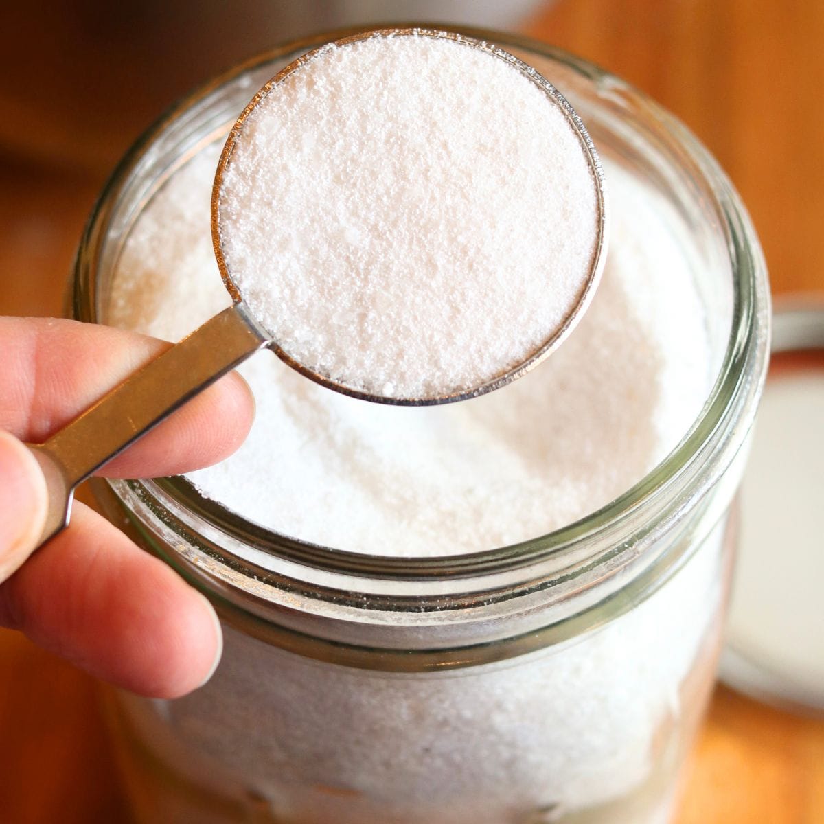 Closeup of tablespoon of homemade dishwasher detergent scooped out of Mason jar.