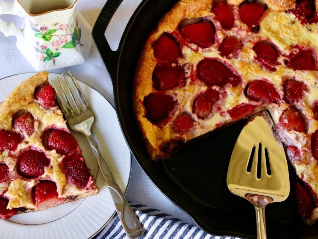 Skillet with strawberry Dutch baby with a slice on a plate.