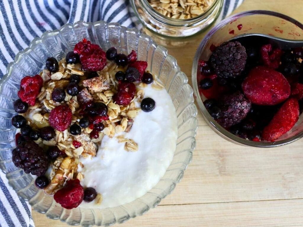 Bowl of coconut yogurt with granola and frozen berries.
