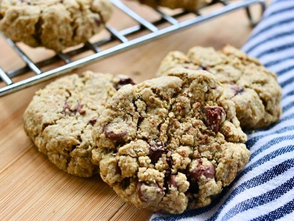 Closeup of oat flour chocolate chip cookie with more cookies on a cooling rack in the background.