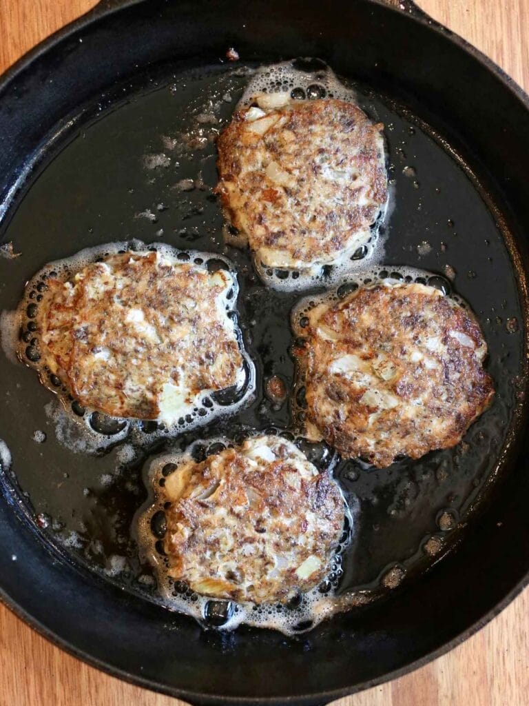 4 sardine fish cakes frying in a cast iron skillet.