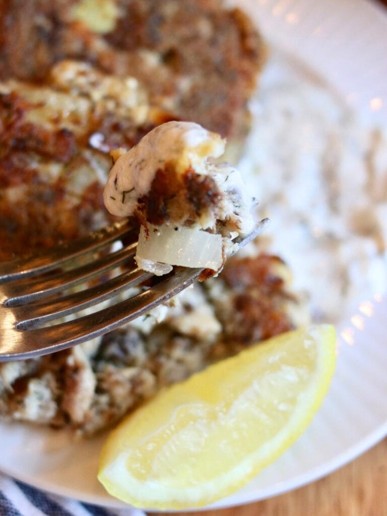 A bite of a sardine fish cake with yogurt dill sauce on a fork.