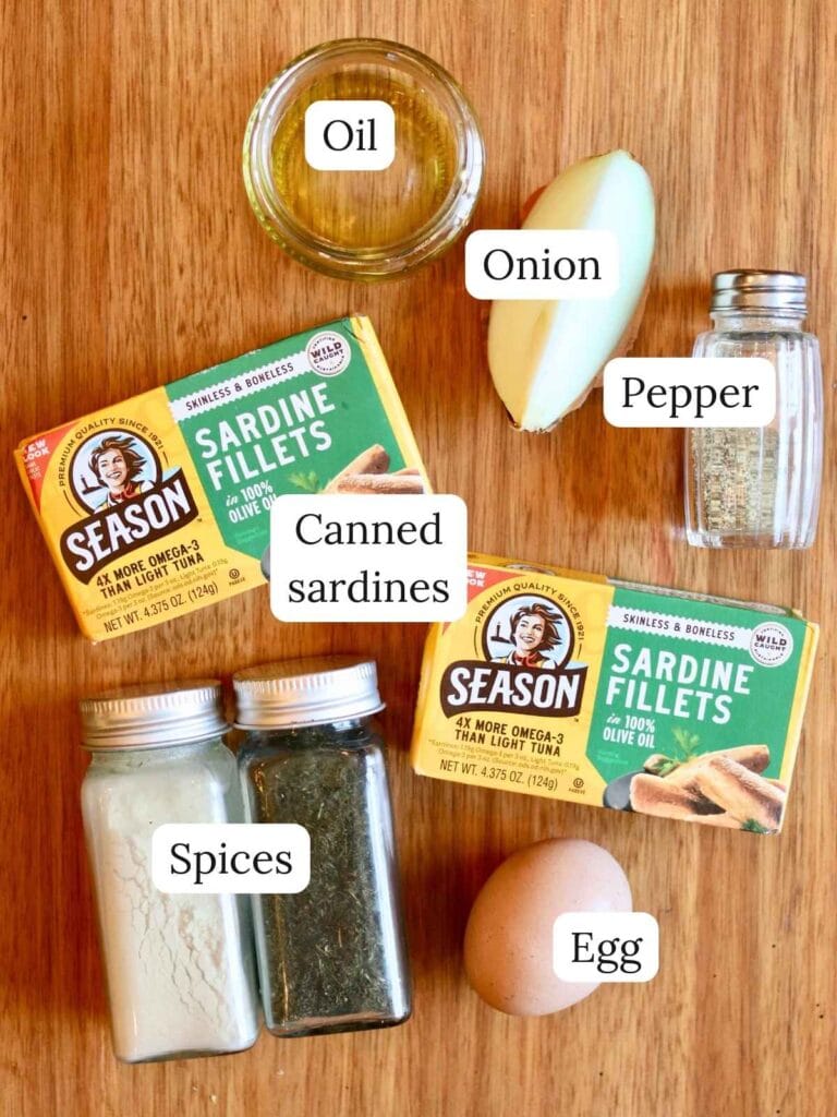 Ingredients for sardine fish cakes including canned sardines, onion, oil, egg, and spices on a wooden surface.