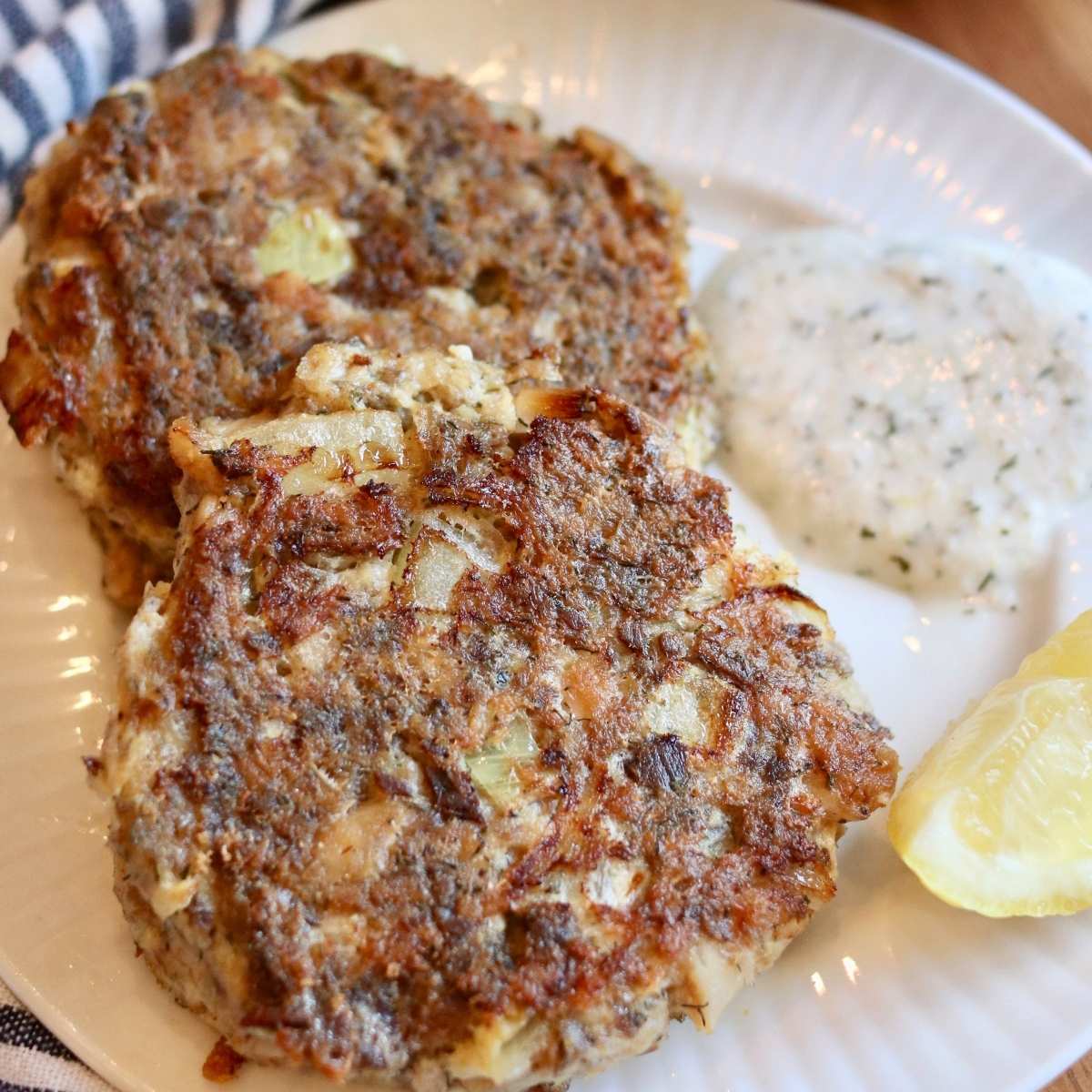 Closeup of 2 sardine fish cakes on a plate with yogurt dill sauce.