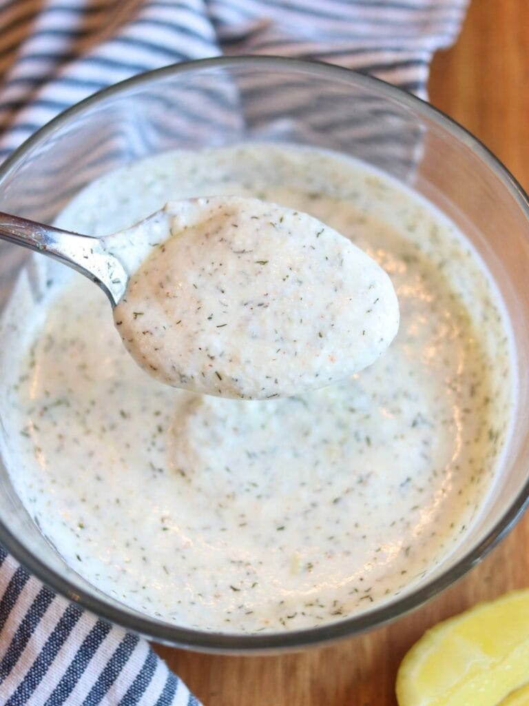 Spoon scooping yogurt dill sauce out of a bowl.