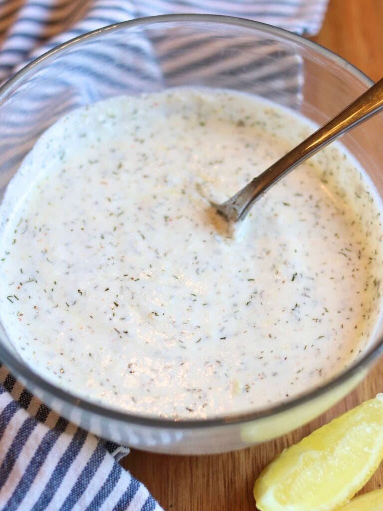 Yogurt dill sauce in a glass bowl with a spoon in it.