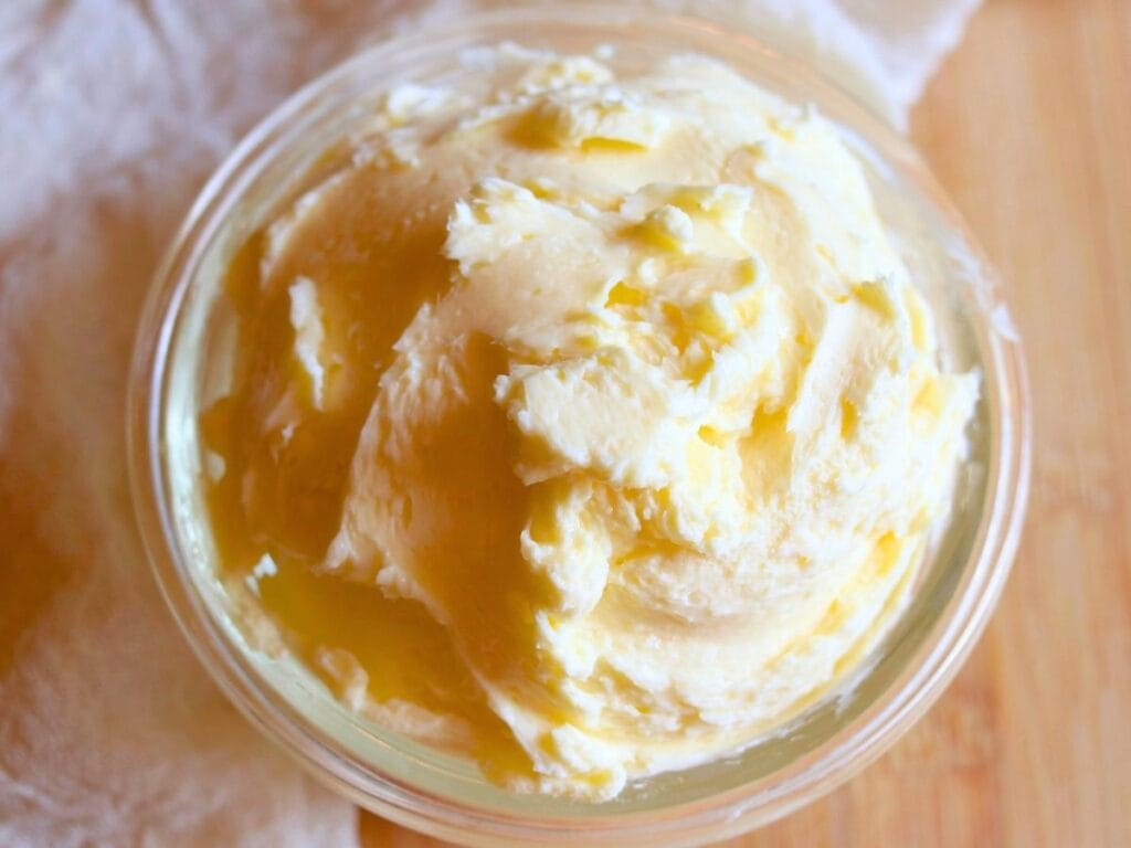 Top view of creamy homemade butter made from raw milk in a glass jar on a wooden surface.