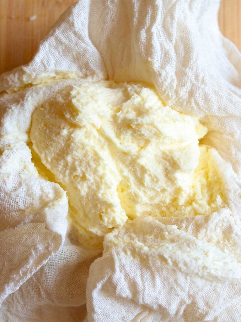Creamy raw milk butter wrapped in cheesecloth after churning in a food processor on wooden surface.
