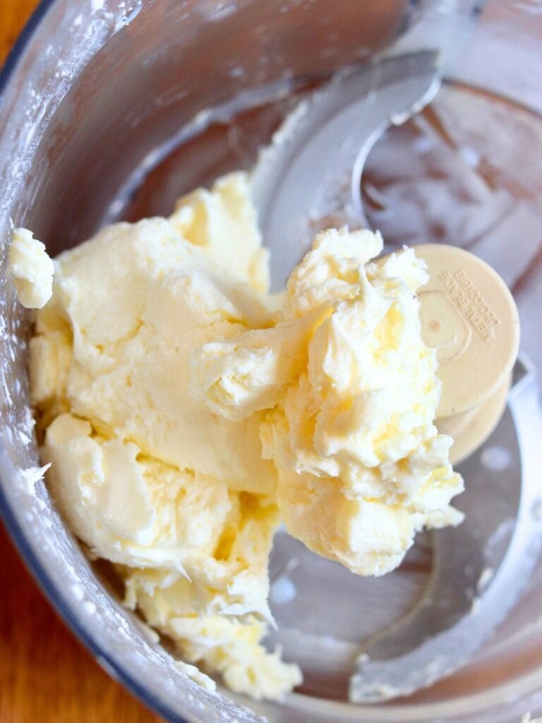 Homemade butter from raw milk in a food processor during churning process on wooden counter.