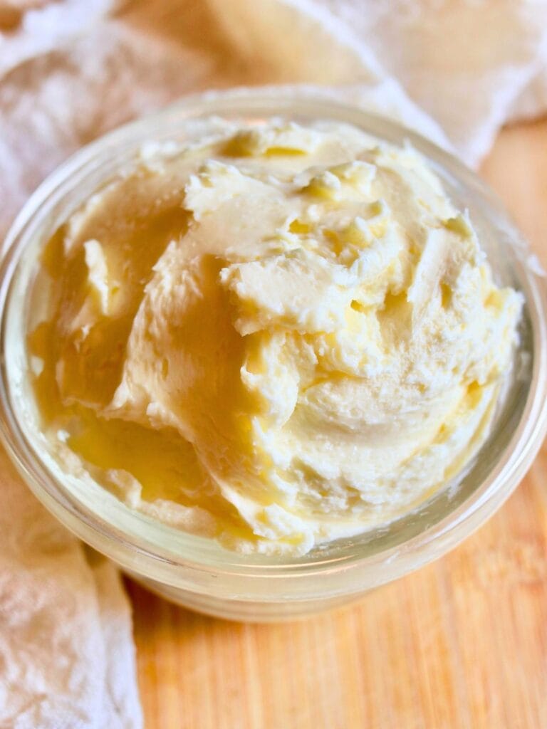 Creamy homemade butter made from raw milk in a glass jar on a wooden table with a cheesecloth.