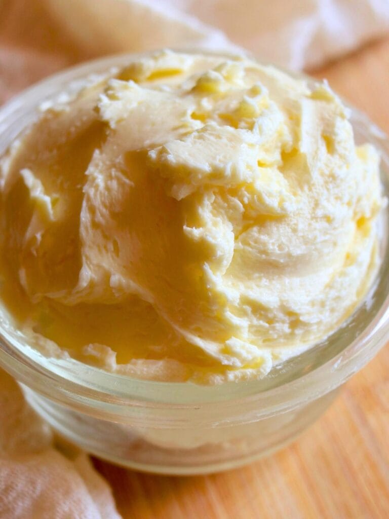Close-up of homemade raw milk butter in a clear glass jar on a wooden surface.