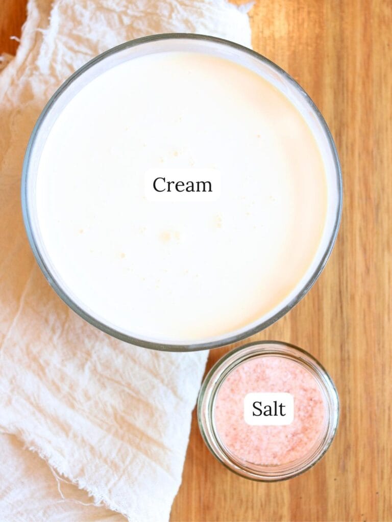 Fresh cream and pink Himalayan salt in glass jars on a wooden surface — ingredients for making homemade butter from raw milk.