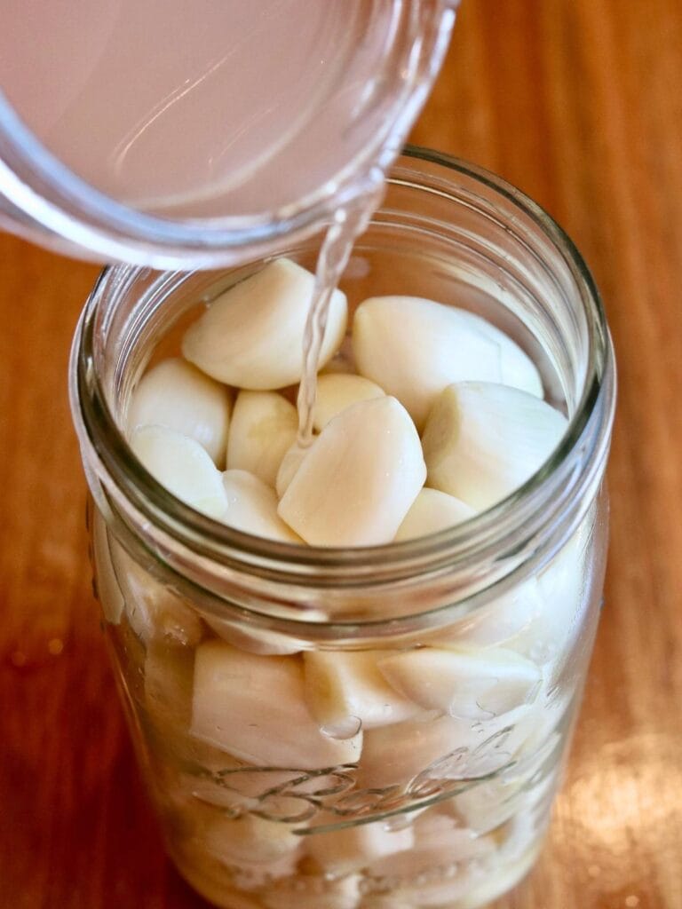 Pouring saltwater over garlic cloves in a jar.