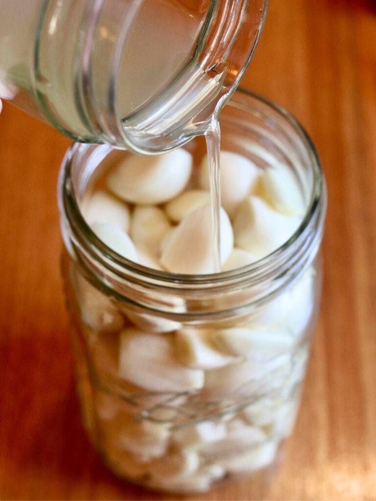 Pouring sauerkraut juice over garlic cloves in a jar.