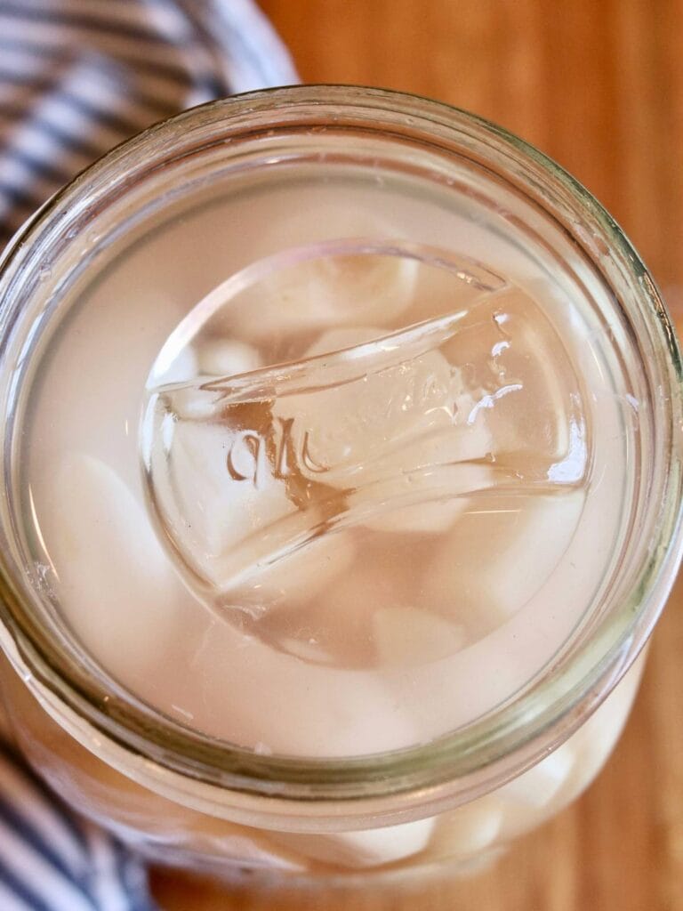 Fermentation weight on top of garlic cloves in a jar.