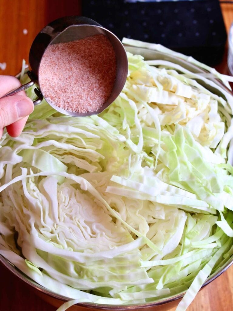 Adding salt to a bowl of sliced cabbage.