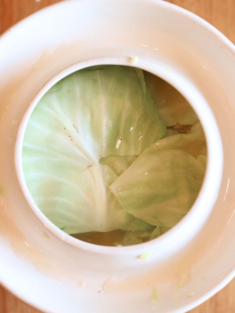Cabbage covered with cabbage leaves in a crock.