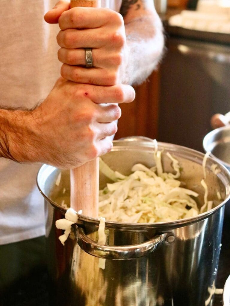 Man pounding sliced cabbage with a cabbage tamper.