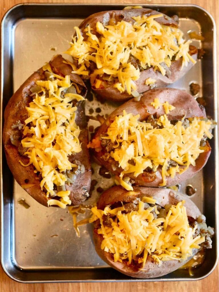 Sweet potatoes on a baking sheet with ground beef and shredded cheese.