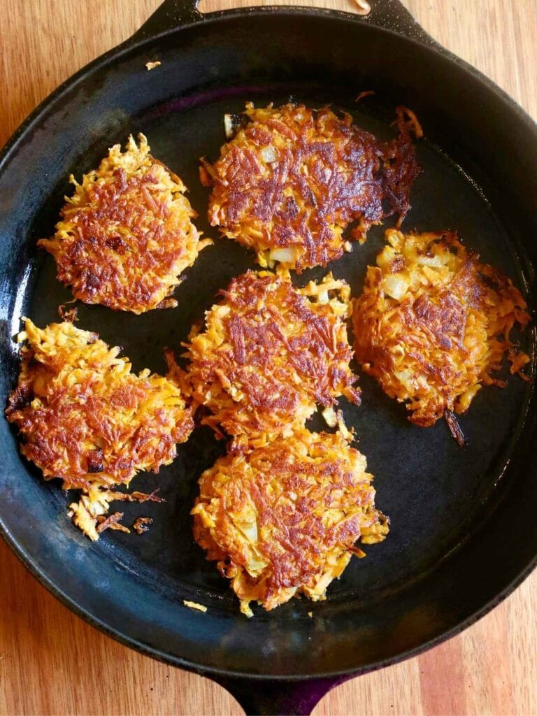 Cooking sweet potato fritters in a hot cast iron skillet until golden brown and crispy on each side.
