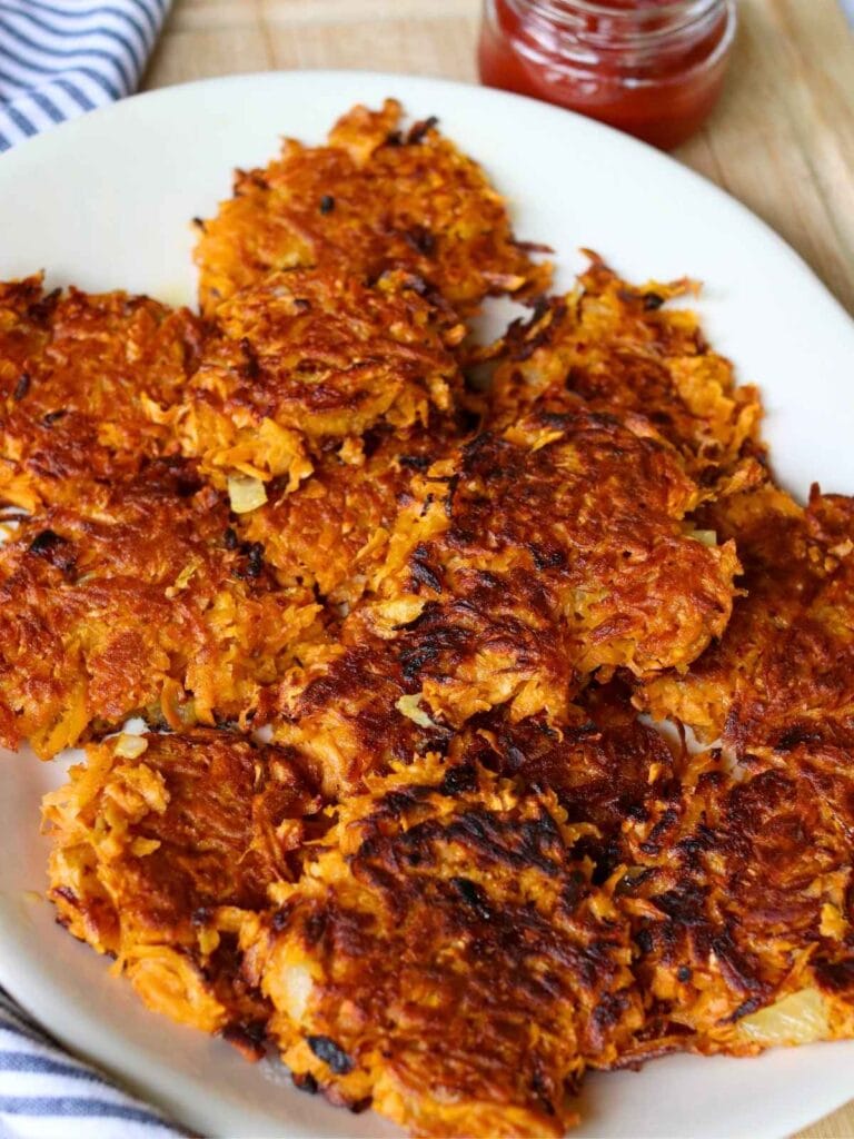 Top view of sweet potato fritters arranged neatly on a serving plate with a side of ketchup as dipping sauce.