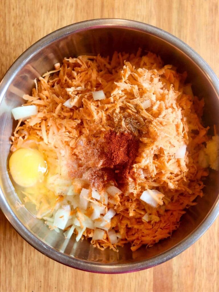 Mixing shredded sweet potatoes with seasonings and egg in a large bowl to prepare fritter batter.