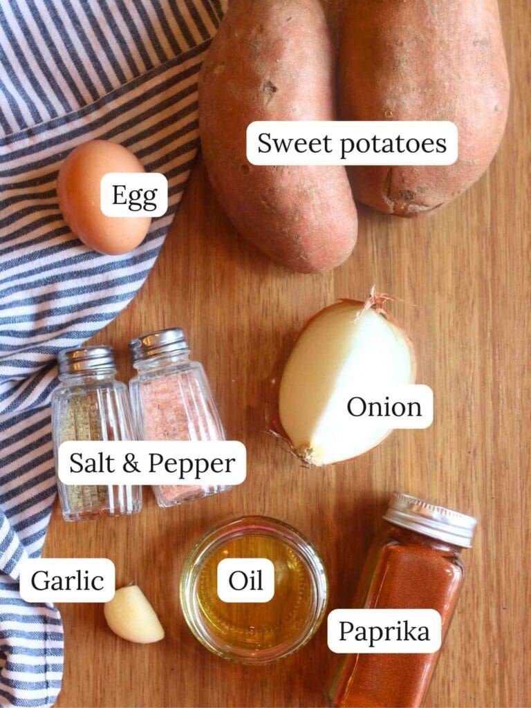 Flat lay of fresh ingredients for sweet potato fritters including shredded sweet potatoes, egg, onion, oil, and seasonings.