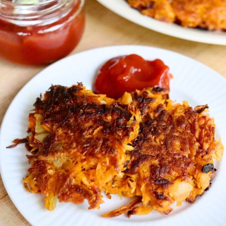 Golden crispy sweet potato fritters served with ketchup on a rustic wooden platter.